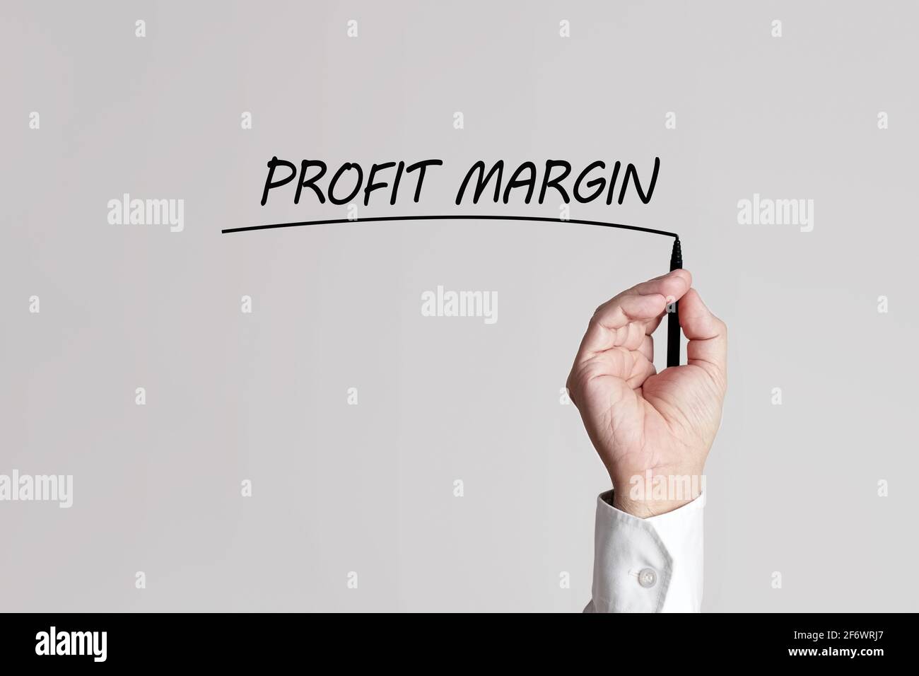 Businessman hand with pen underlines the words profit margin on a gray background virtual screen. Stock Photo