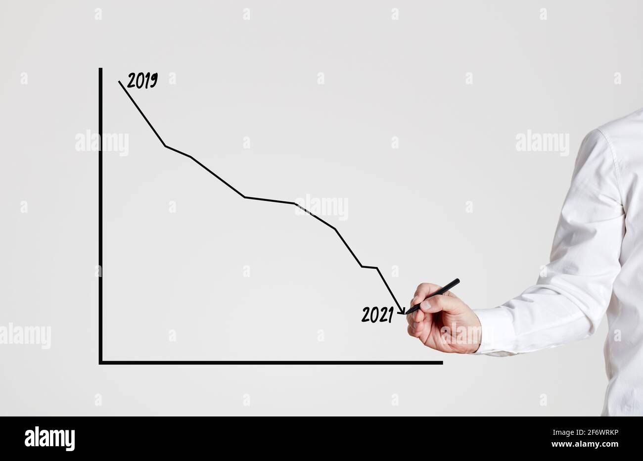 Businessman draws a declining line graph between the years of 2019 and 2021. Negative financial impact of coronavirus pandemic on economy and business Stock Photo