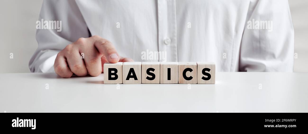 Businessman pressing his finger on the wooden cubes with the word basics. Back to basics, simplification in business or education concept. Stock Photo