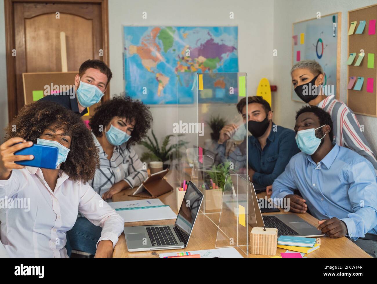 Young people in co-working creative space wearing surgical mask and taking selfie with mobile smartphone - Health care and business technology concept Stock Photo