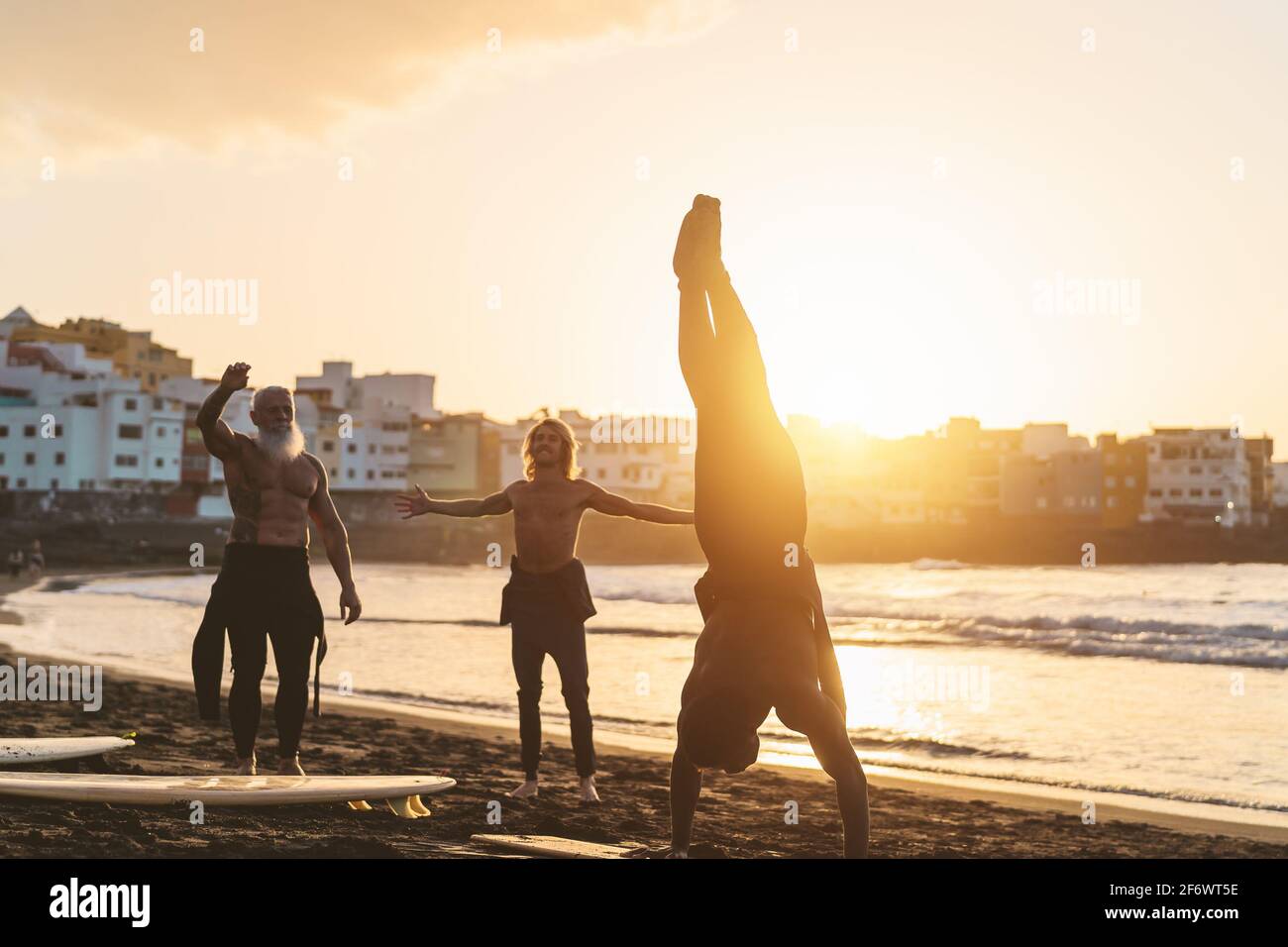 Happy fit surfers with different age and race doing warm up exercises before surfing during sunset time Stock Photo