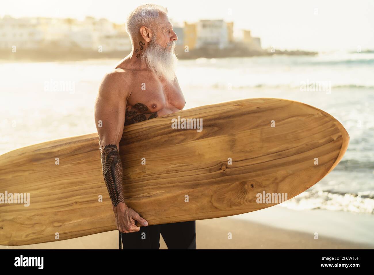 Fitness senior having fun surfing at sunset time - Sporty bearded man training with surfboard on the beach Stock Photo
