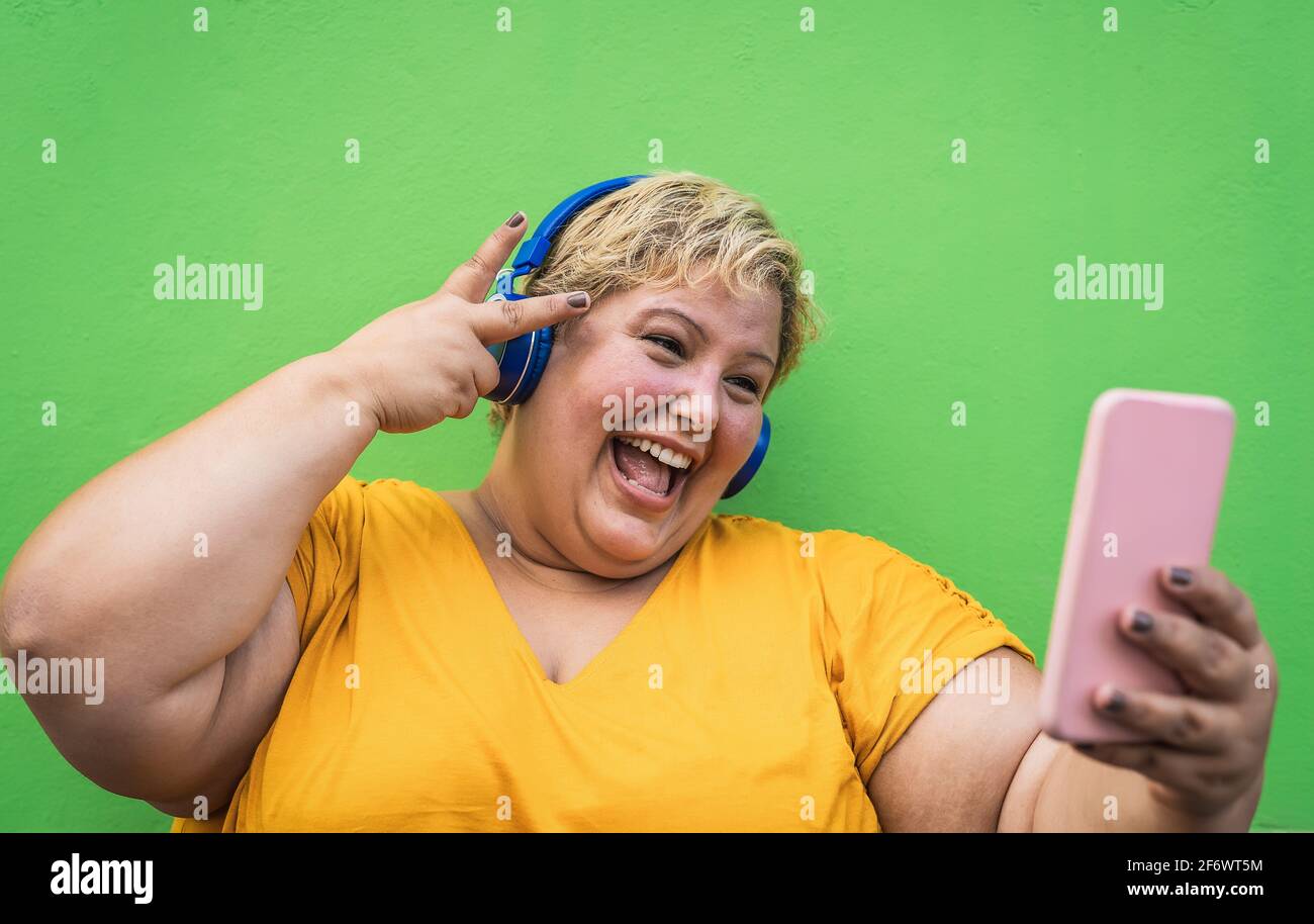 Happy plus size woman taking selfie with mobile smartphone and listening music with wireless headphones Stock Photo