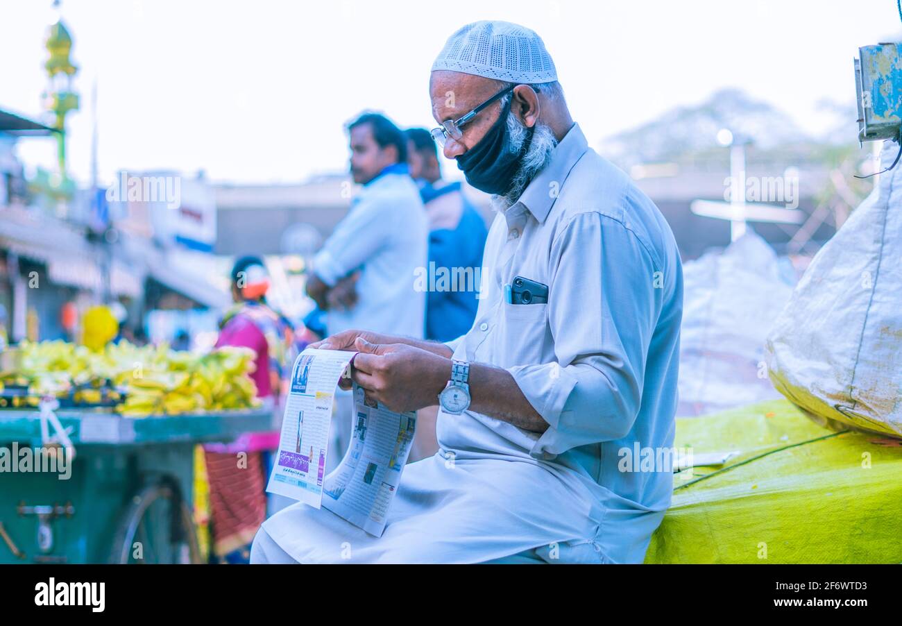 K.R.Market, Bangalore, India - February 06,2021: Old muslim person reading news paper on the streets of K.R.Market Stock Photo