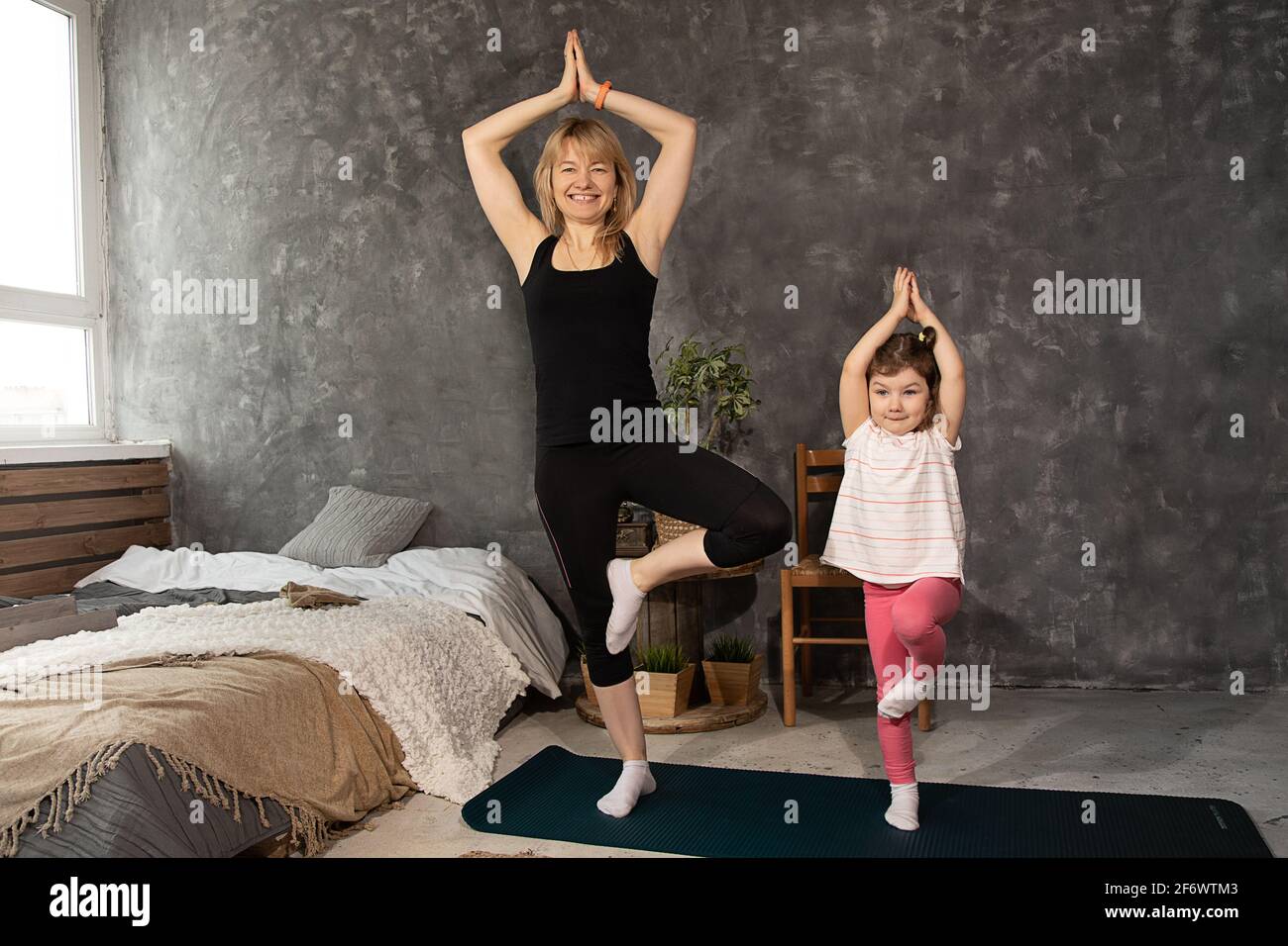 Young woman and child daughter doing yoga exercise and stretching at home. Health, sport, leasure concept. mother and little girl practicing together Stock Photo