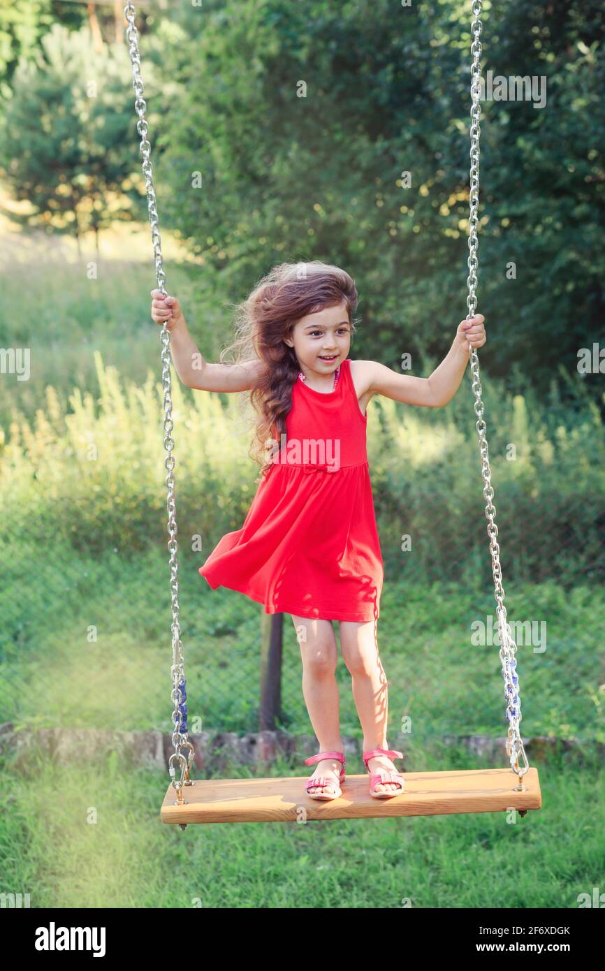 Beautiful little girl is swinging and smiling at summer day, Happy childhood concept Stock Photo