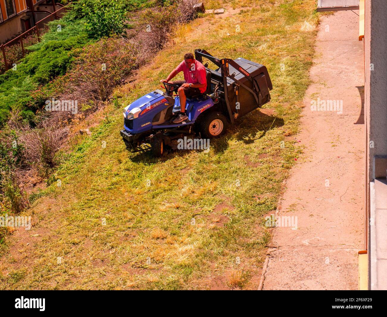 Usti nad Labem / Czech republic - 06.25.2019: A man on a small tractor cutting the grass on a small strip of lawn, in front of the residential house Stock Photo