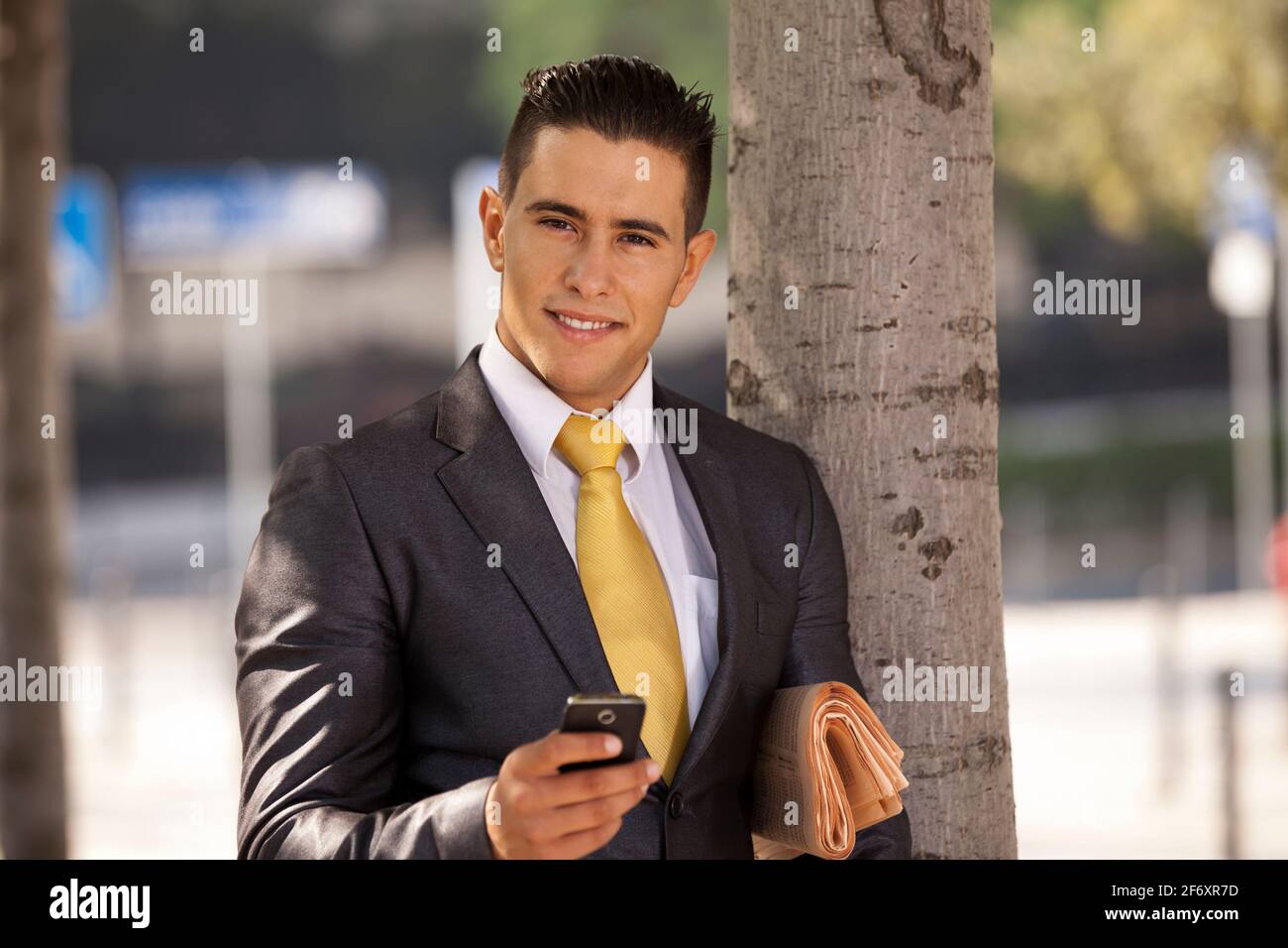 Businessman relaxing next to a tree at the city park, sending short ...