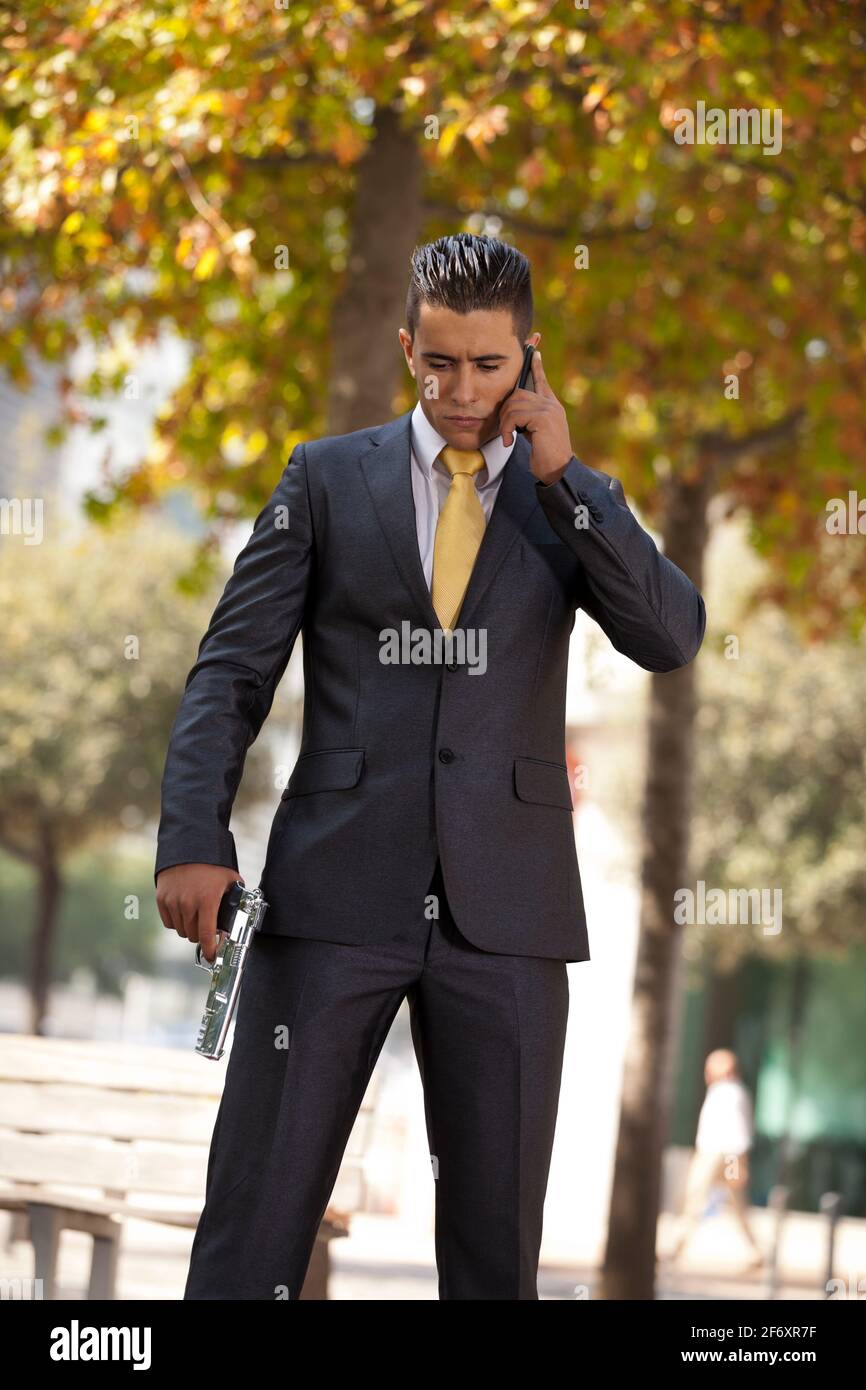 Powerful security businessman talking at his cellphone with a handgun in his hand Stock Photo
