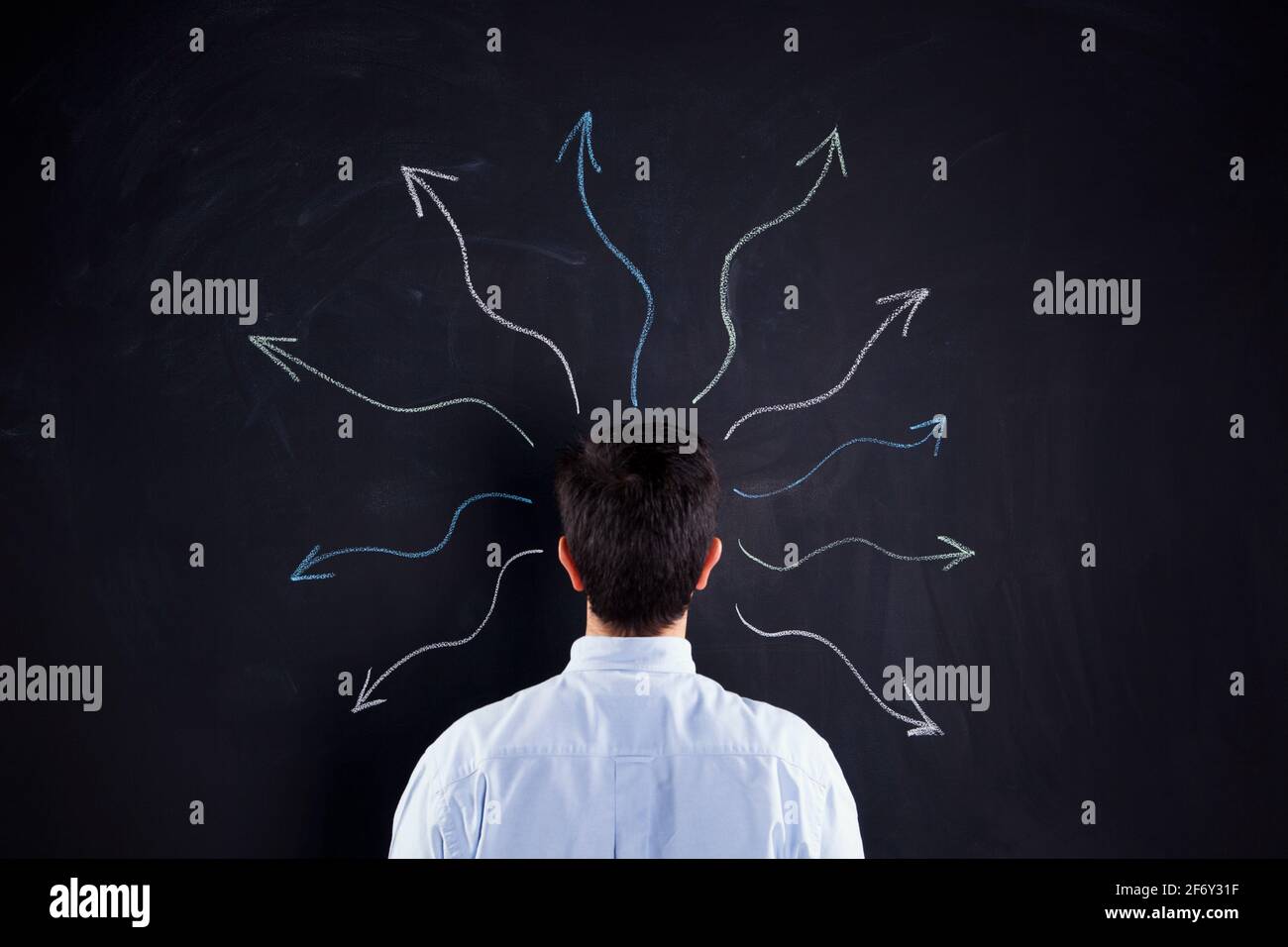 Businessman looking to a chalkboard with lots of arrows flowing from his head Stock Photo