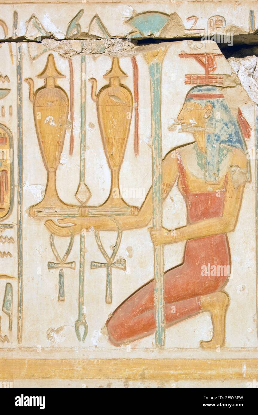 An ancient egyptian hieroglyphic carving showing the goddess Isis in a red dress and holding two jars of wine together with sacred ankhs. Wall of the Stock Photo
