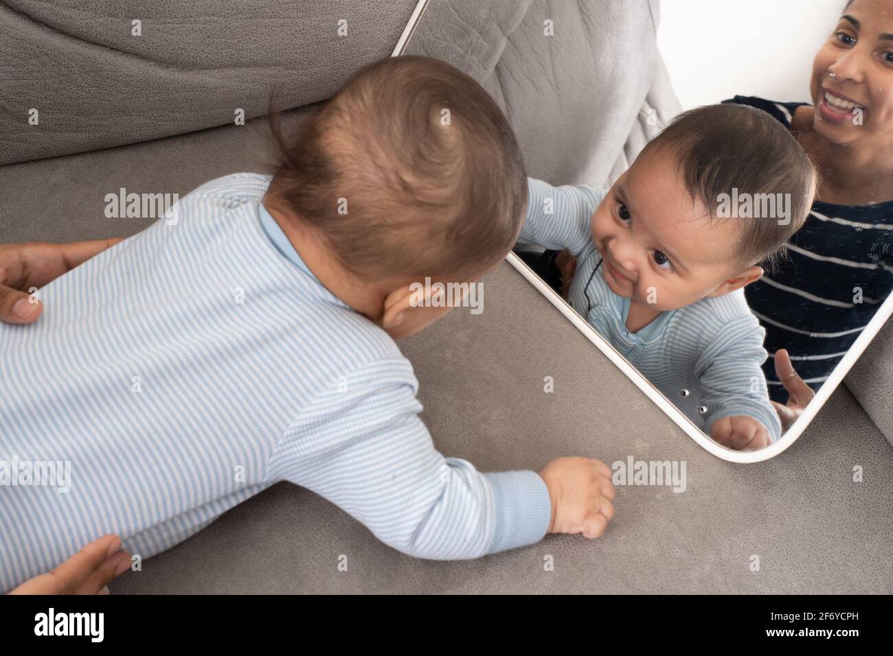 4 month old baby boy looking at self in mirror, mother in background Stock Photo