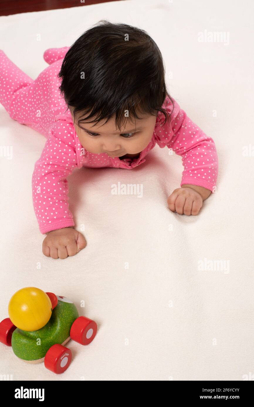4 month old baby girl on stomach holding head up, looking intently at wooden toy duck Stock Photo