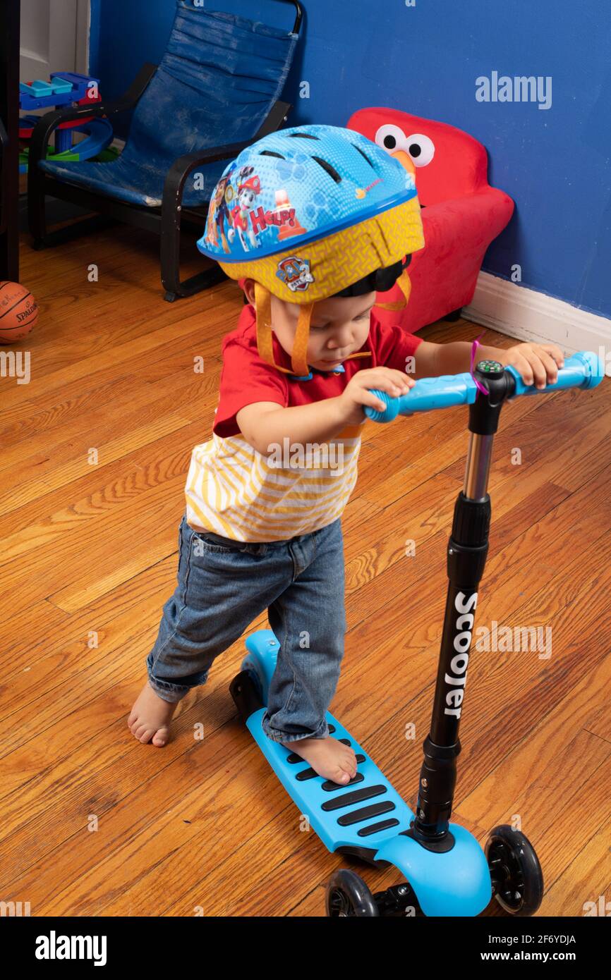 Two year old boy in safety helmet riding scooter in bedroom Stock Photo