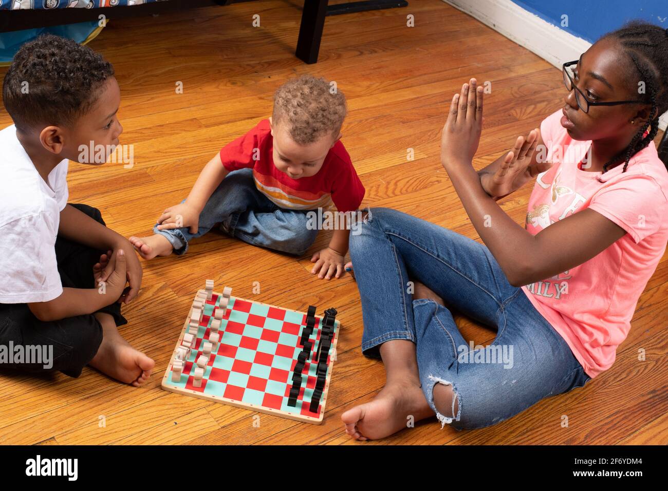 11 year old girl teaching her 6 year old brother how to play chess, 2 year old brother looking on, discribing how pieces can move with gesture in the Stock Photo