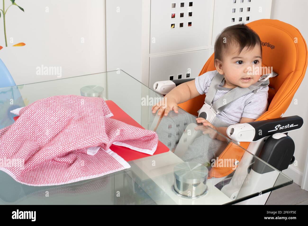 8 month old baby boy sitting in high chair at table Piaget Object Permanence sequence #2 looking away after toy is hidden by cloth lack of object perm Stock Photo