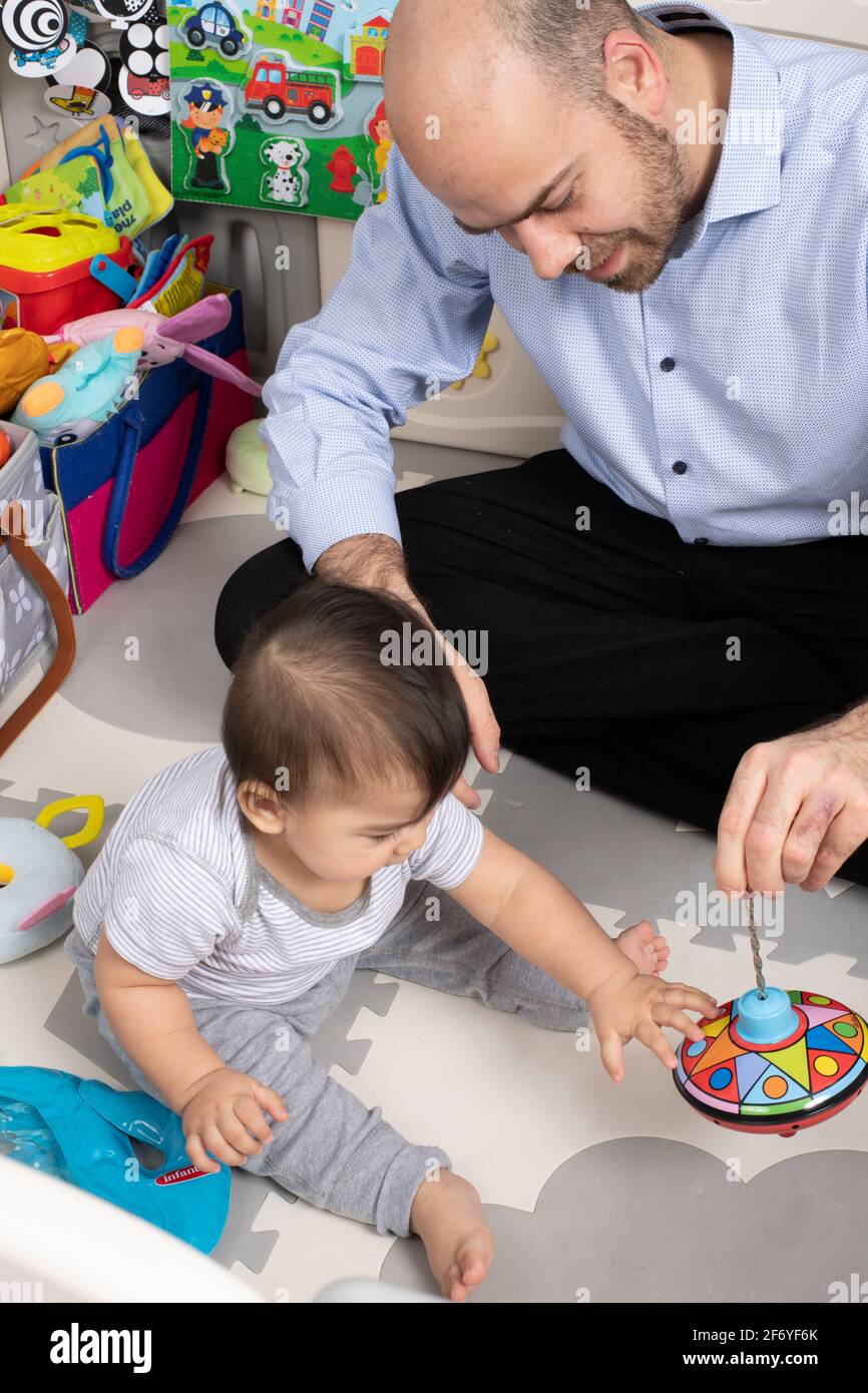 8 month old baby boy, shown new toy by father, father pushing down to spin metal top Stock Photo