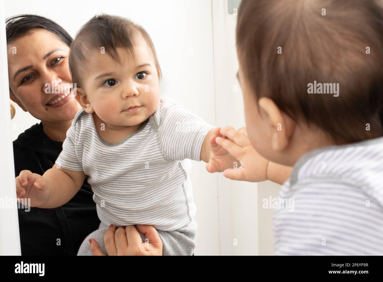 8 month old baby boy with mother looking at reflection in mirror, does not know baby in mirror is himself Stock Photo
