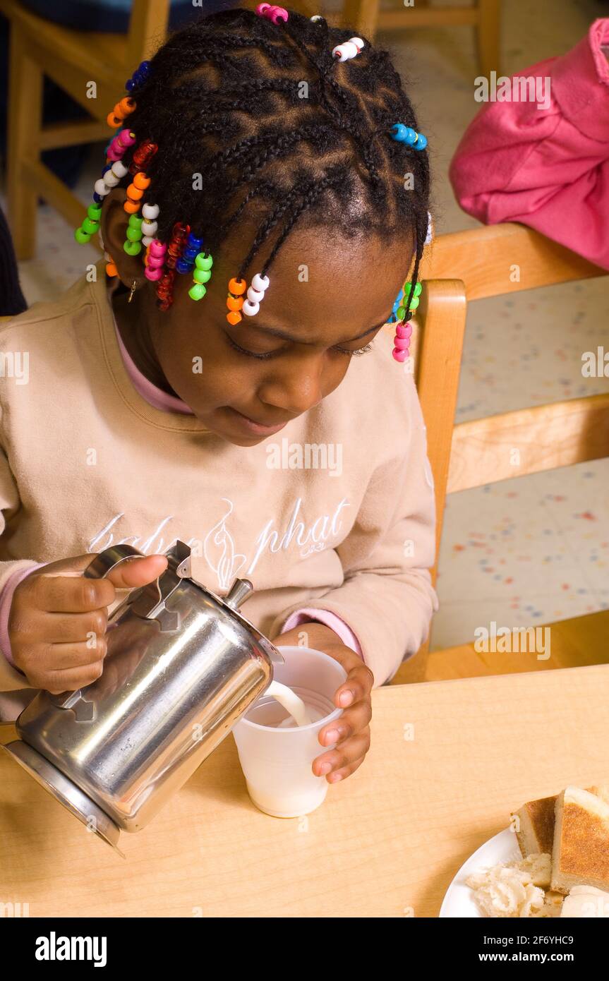 Preschool classroom 3-4 year olds girl pouring own milk at meal time Stock Photo