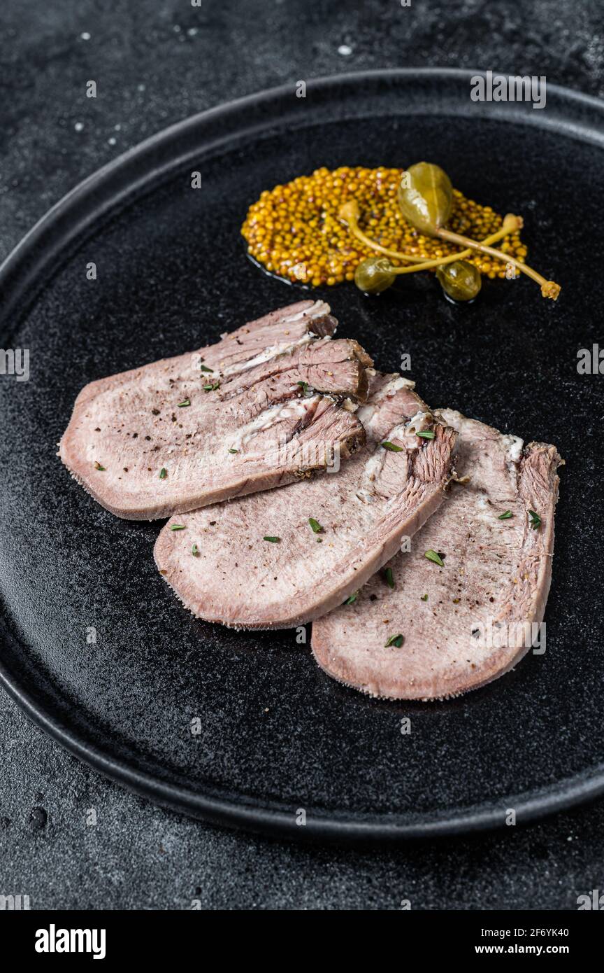 Pork boiled tongue slices on a plate. Black background. Top view Stock Photo