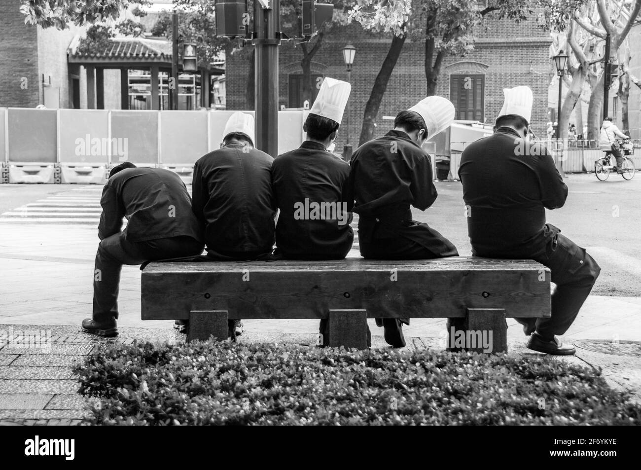 Five chefs fanned out on a bench while taking a break in Shanghai’s Xintiandi. Huangpu District, Shanghai, China. Stock Photo