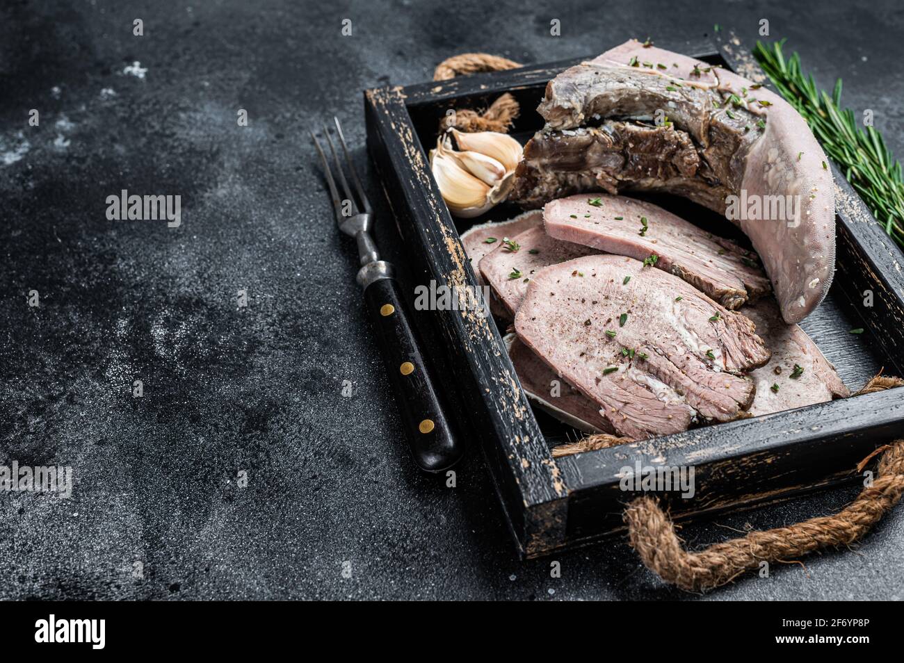 Cooked Boiled veal or beef tongue sliced in a wooden tray. Black background. Top view. Copy space Stock Photo