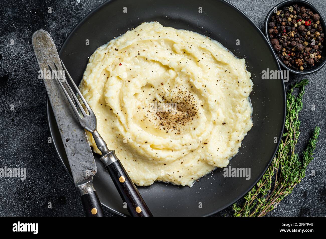 Potato puree, Mashed potatoes in a plate with herbs. Black background. Top view Stock Photo