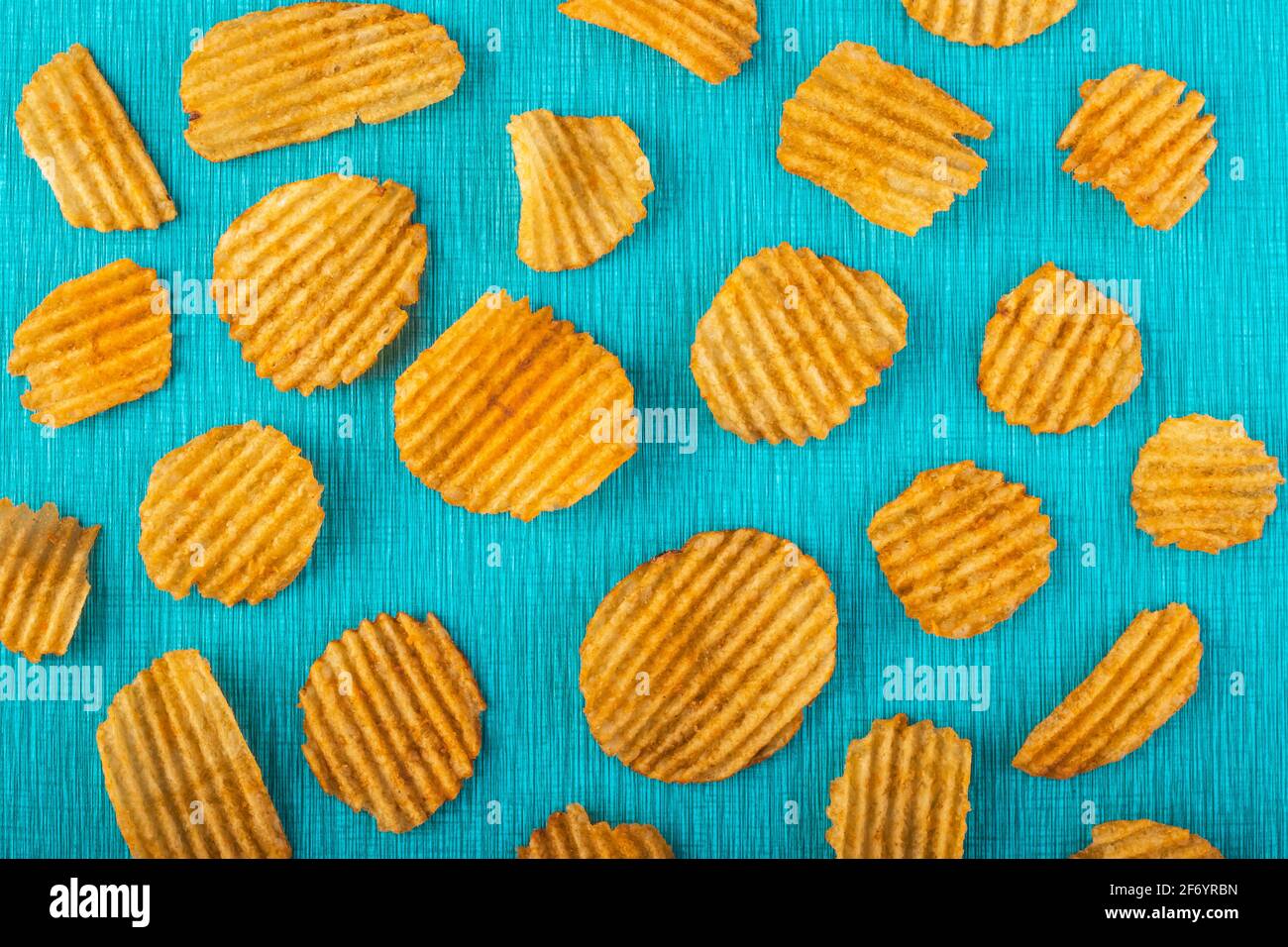 Potato chips, grooved gold chips, corrugated crispy snacks on a turquoise background, colored pattern. Unhealthy fast food. Salted slices texture. Hig Stock Photo