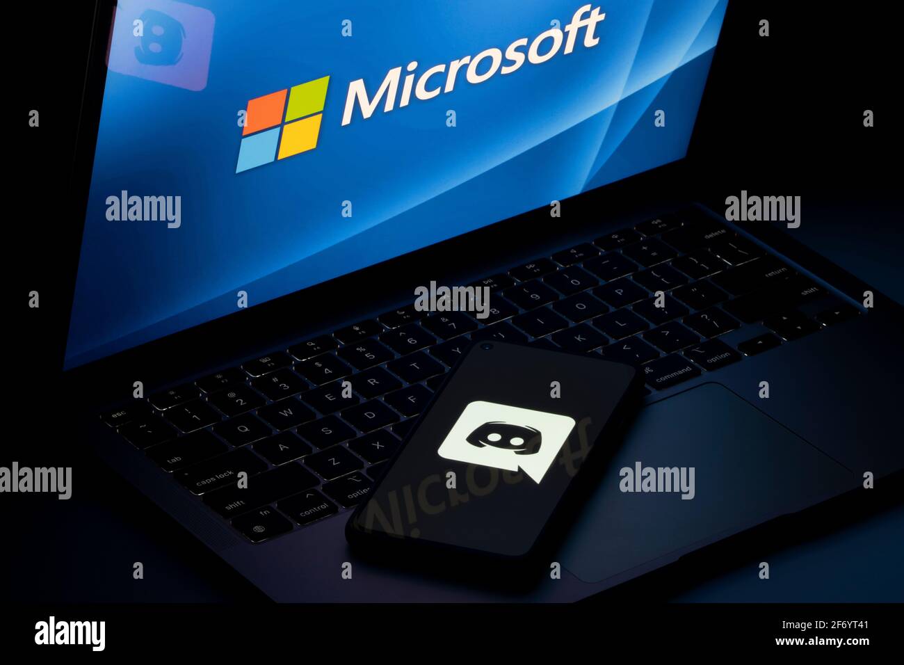 Discord app icon is seen on a smartphone with Microsoft logo on laptop screen in the background. Microsoft is in talks to acquire Discord, a video game... Stock Photo