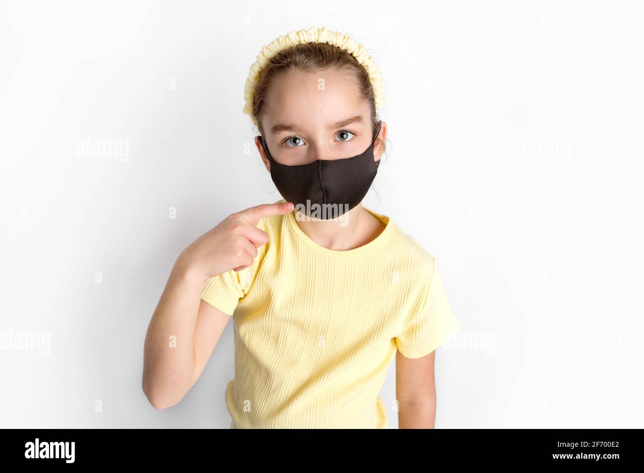 A schoolgirl in a black protective mask draws attention to the correctness and compulsory wearing of protective masks.  Stock Photo