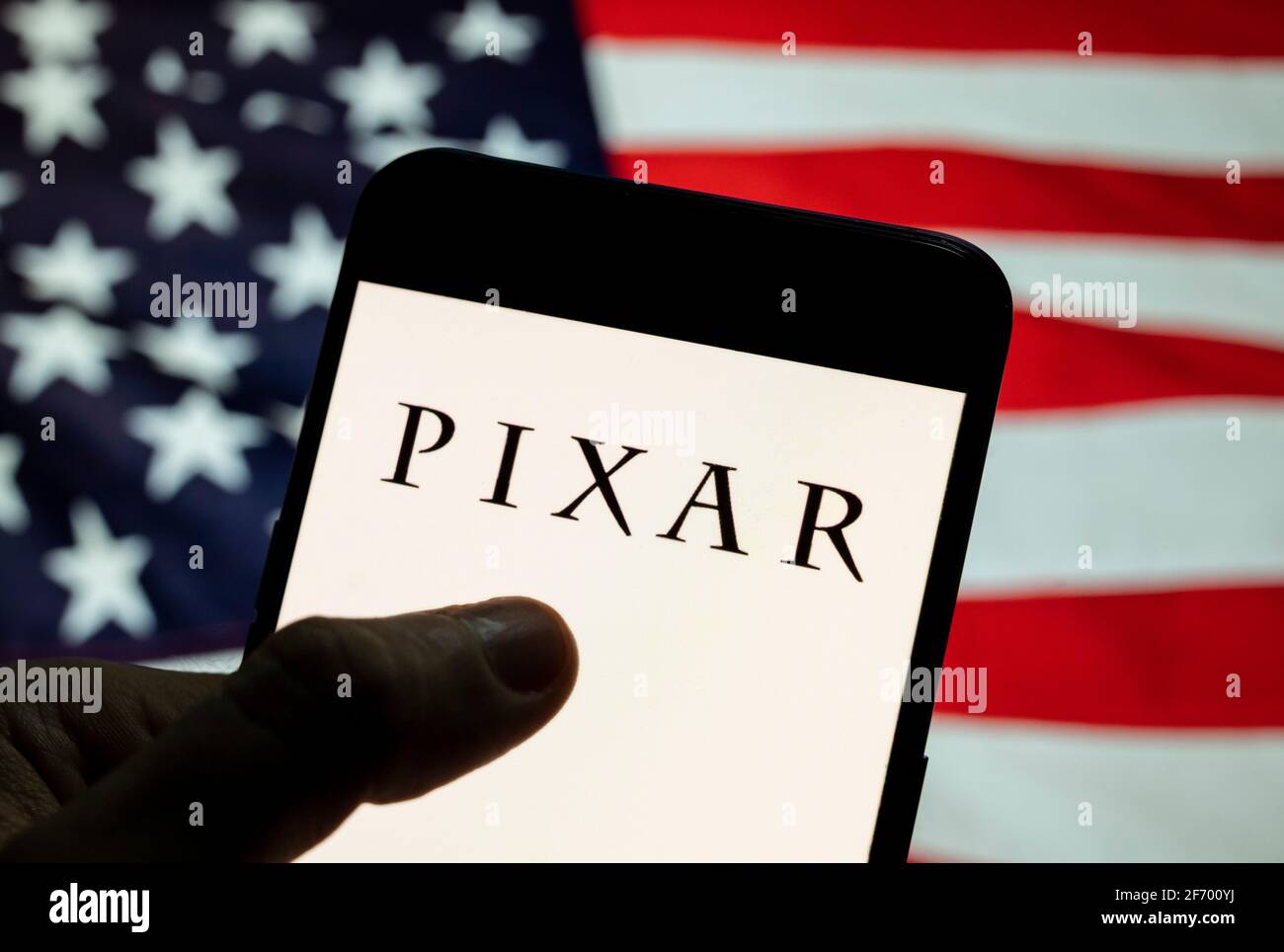 In this photo illustration the American computer animation film studio  owned by Disney, Pixar logo seen displayed on a smartphone with a flag of  the United States in the background Stock Photo -