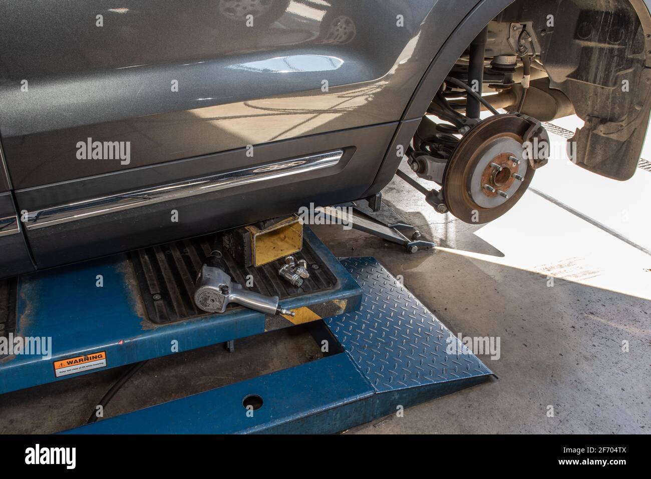 Impact wrench lays on vehicle lift with wheel off exposing rotor during