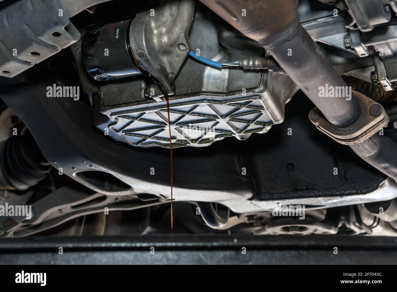 Oil drains from from beneath vehicle during a routine maintenance fluid change at mechanic garage. Stock Photo