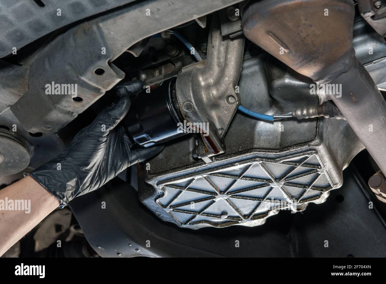 Oil drains from from beneath vehicle as mechanics gloved hand removes
