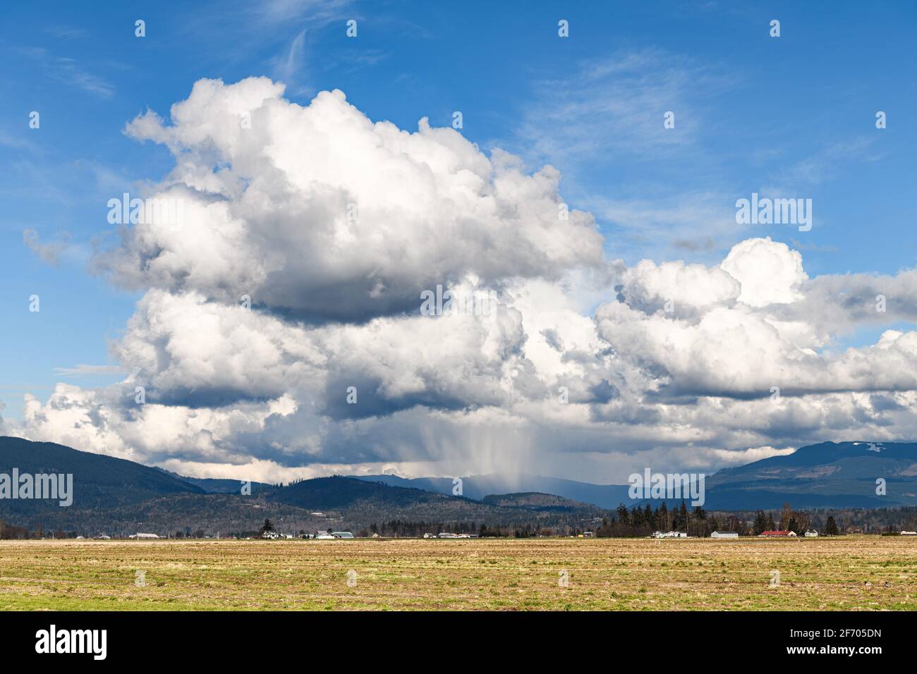 Rain clouds on a late winter day in the Skagit Valley of Washington State with rain falling in a shaft in front of the Cascade Mountains foothills Stock Photo