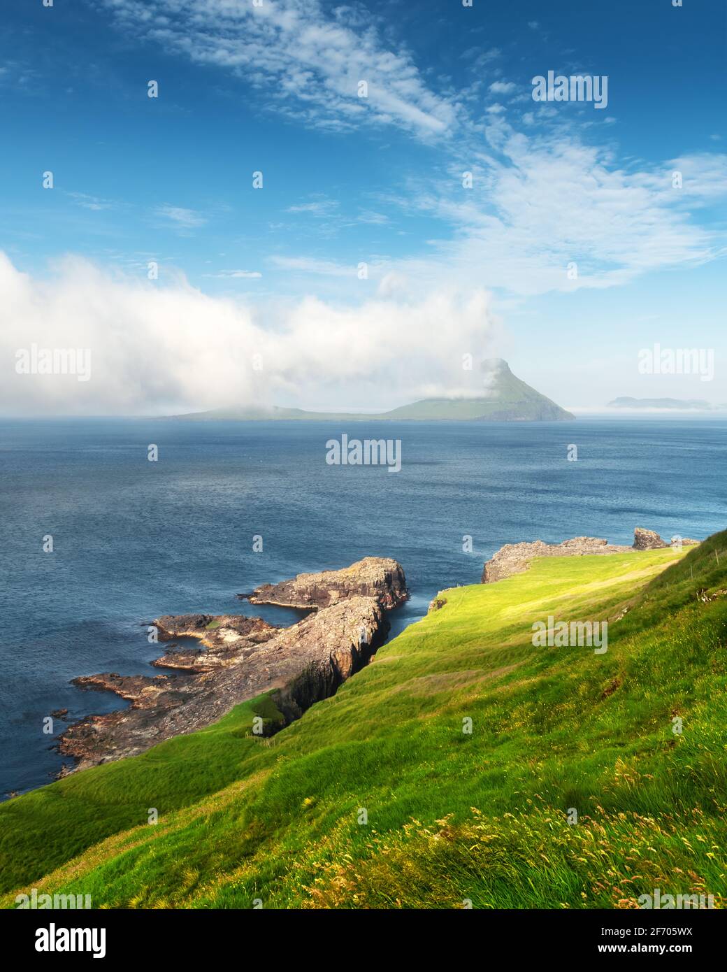 Morning view onto the Faroese island Koltur with spectacular clouds and blue water in a dramatic valley with mountain range. Faroe Islands, Denmark. L Stock Photo