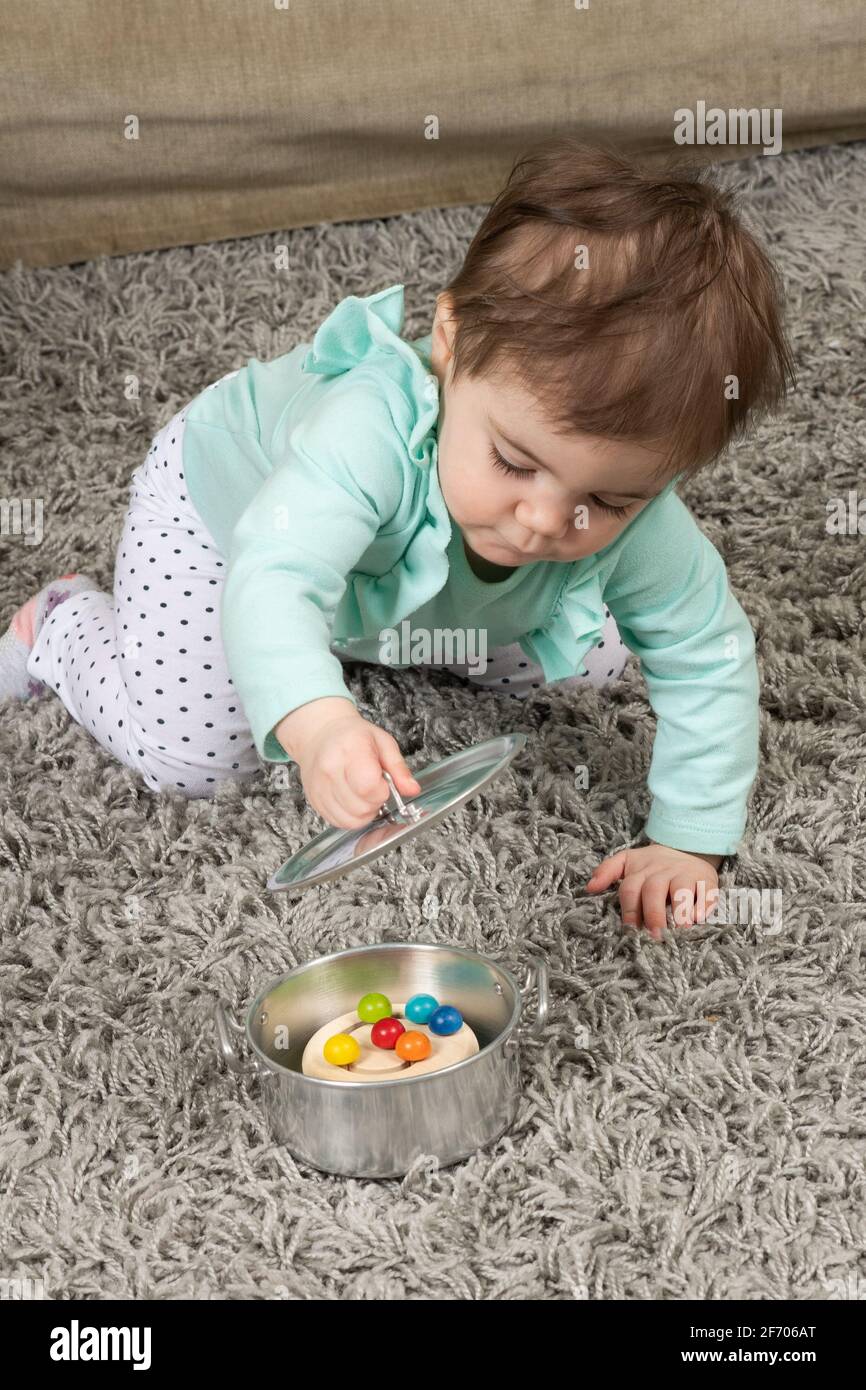 10 month old baby girl opening lid on pot to find hidden toy Piaget object permanence Stock Photo