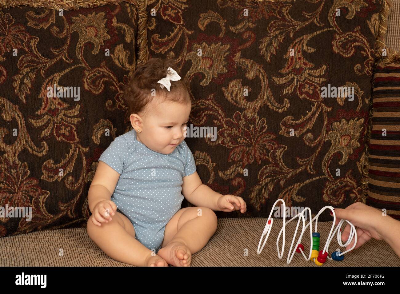 7 month old baby girl sitting on couch interested in wire bead toy Piaget Object Permanence series 1 of 2 Stock Photo