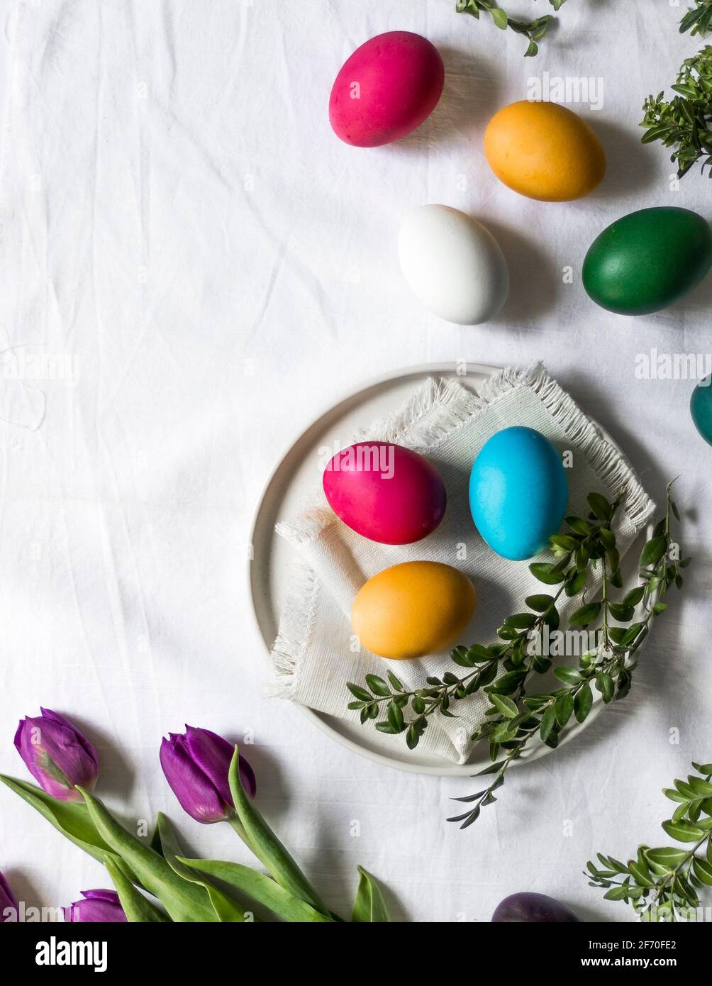 Easter scene - painted eggs lying on tablecloth, on the kitchen table next to fresh purple tulips, ready to be placed in Easter basket. Stock Photo