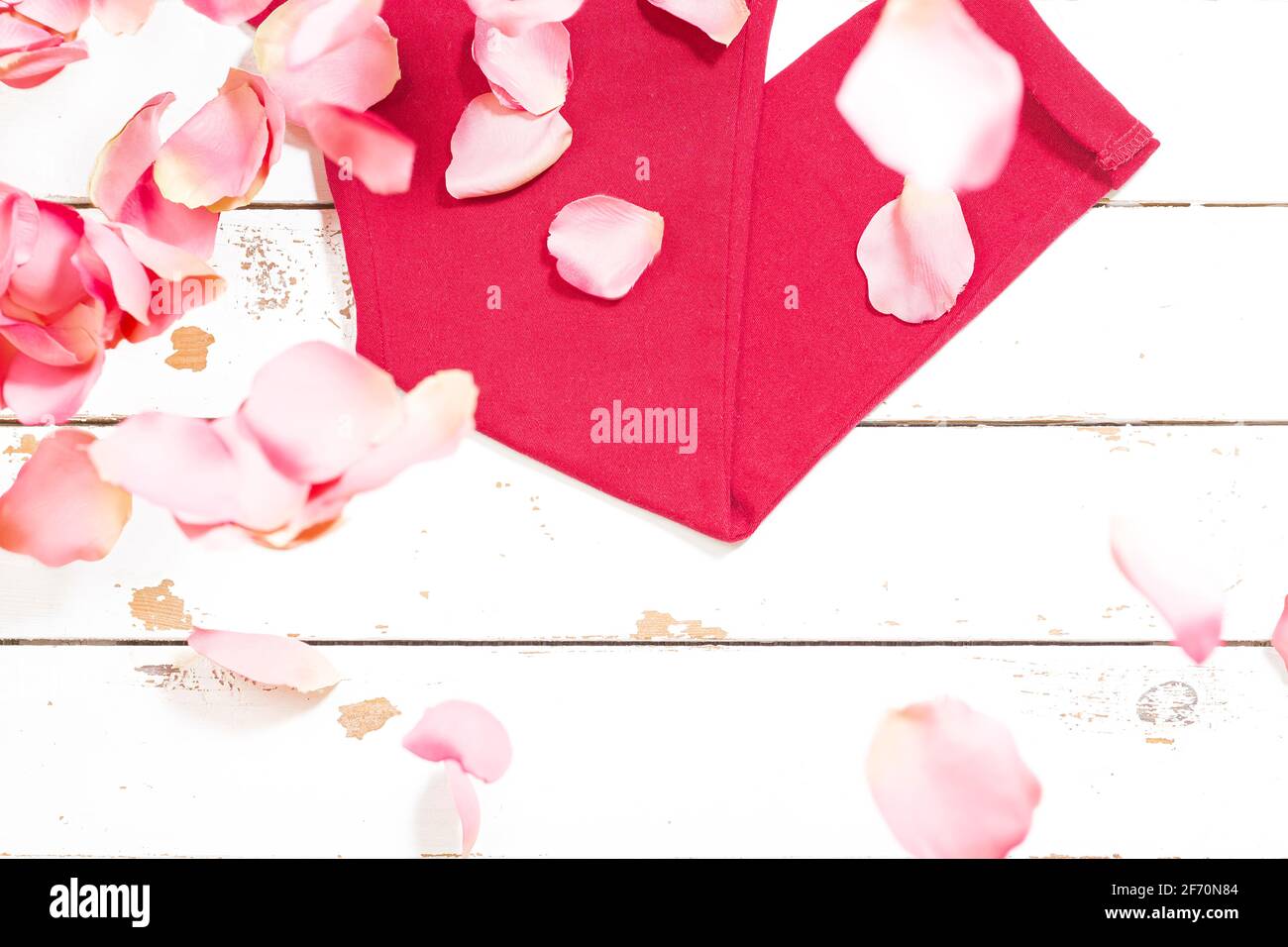 Photograph of clothes of a red pants on white wood and some rose petals. The photograph is an overhead shot with a horizontal format. Stock Photo