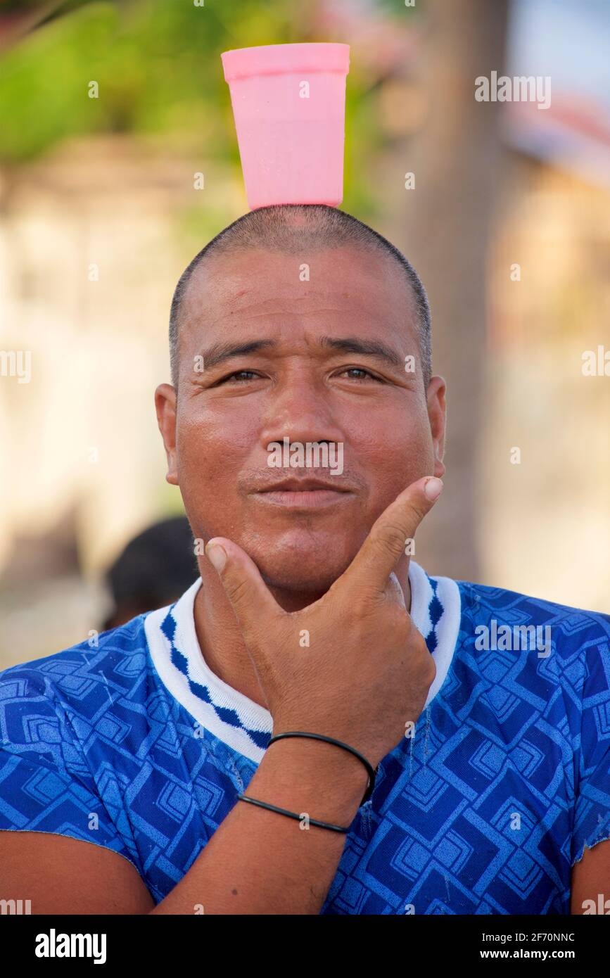 Confident Filipino man holding a contemplative pose whilst holding a pink plastic cup with beverage drink on his head. Bantayan Island, Cebu, Philippines. Stock Photo