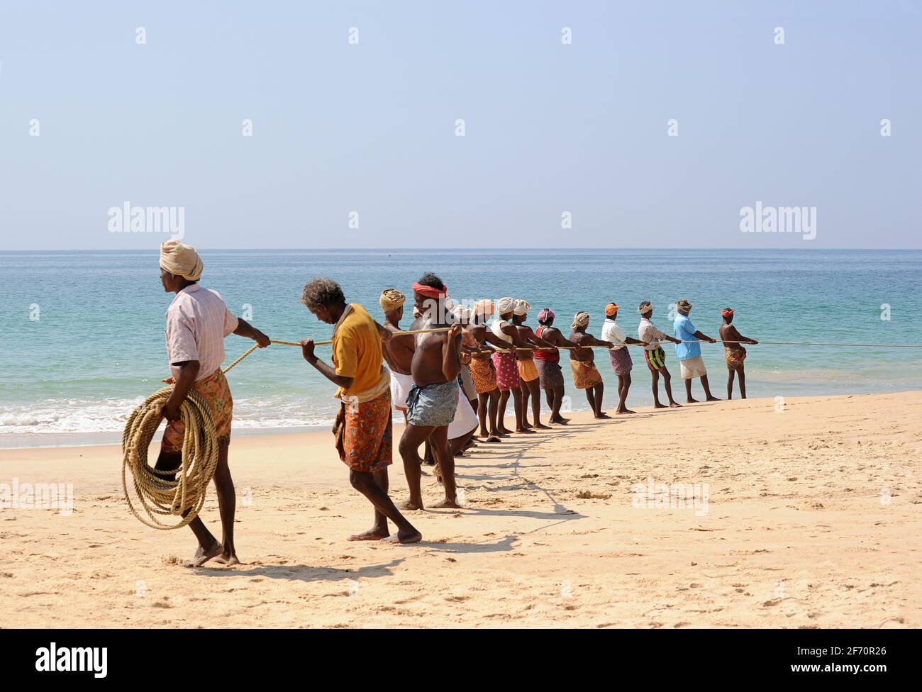 Indian fisherman with a rope pulling in a boat (off picture) to shore.  Trivandrum, Kerala, India Stock Photo