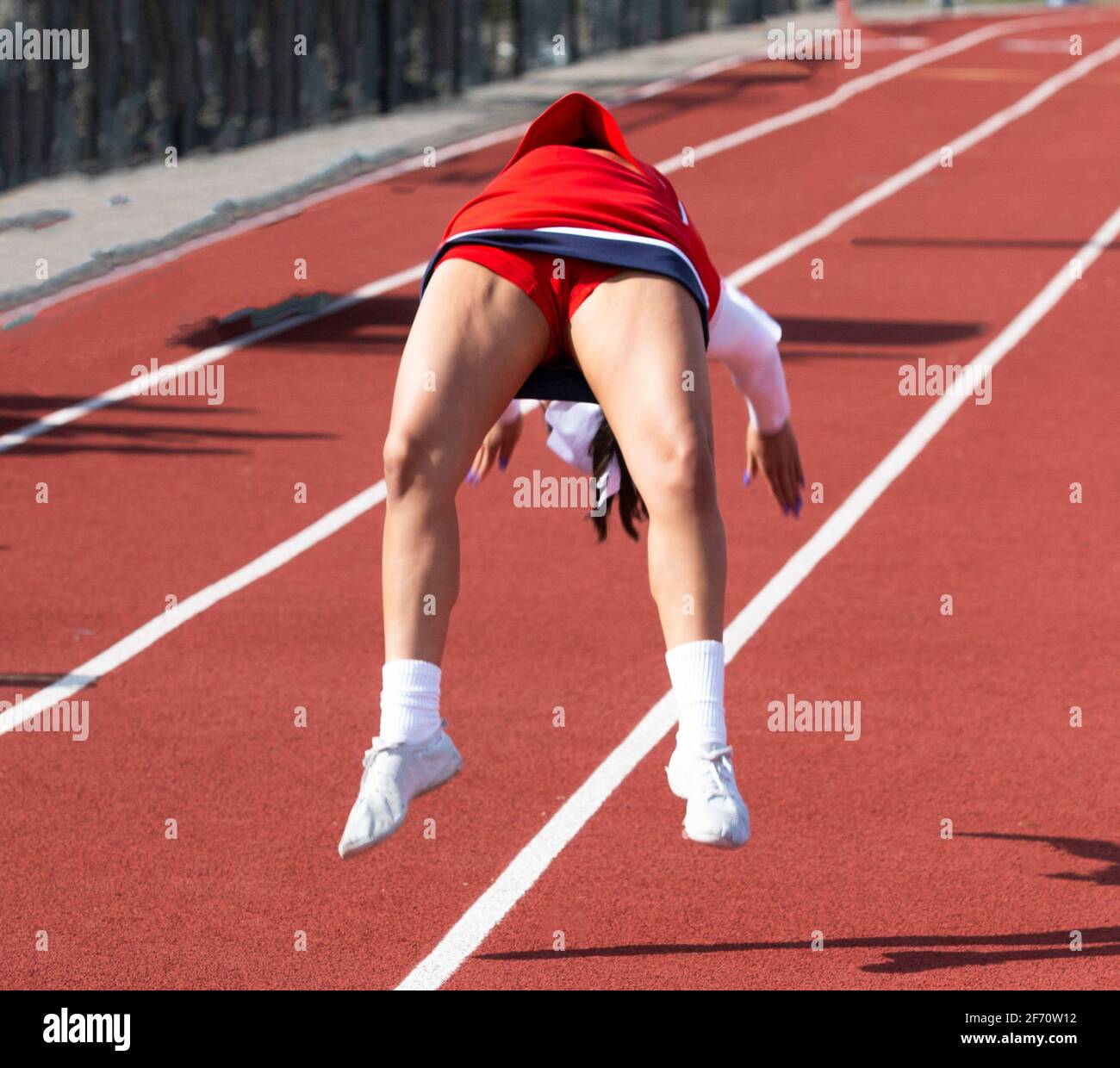 A high school cheerleader performs flips on a red track during a break in a football game. Stock Photo