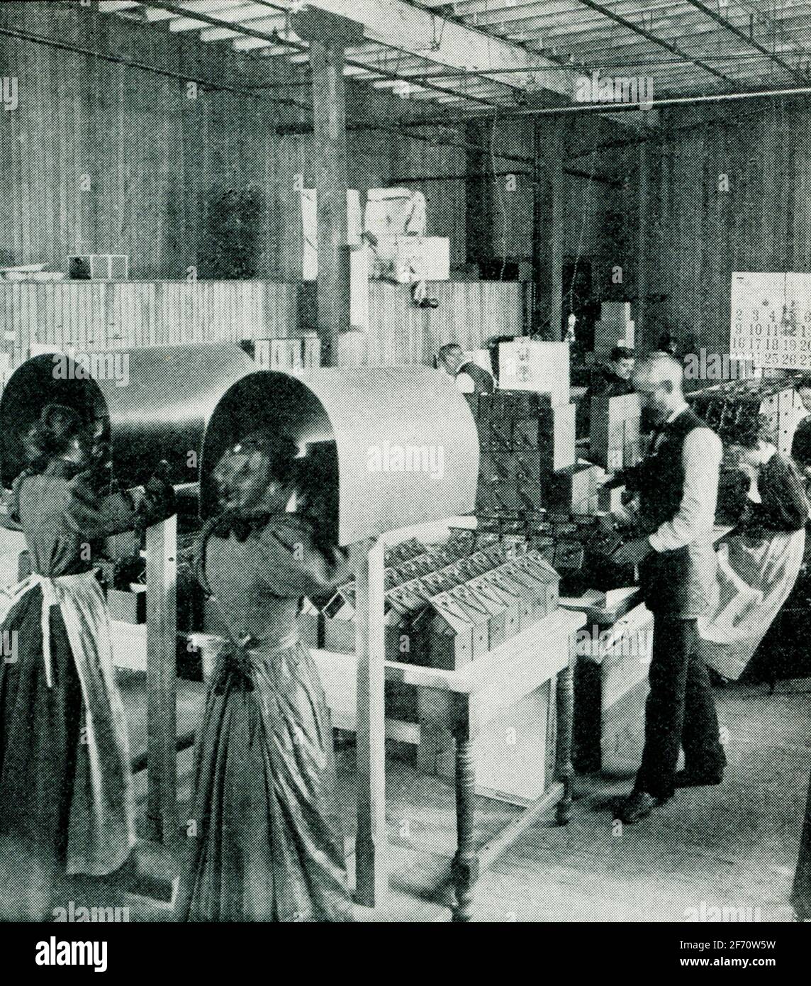 This 1903 photo shows the inside of a camera factory with workers testing lenses. Stock Photo