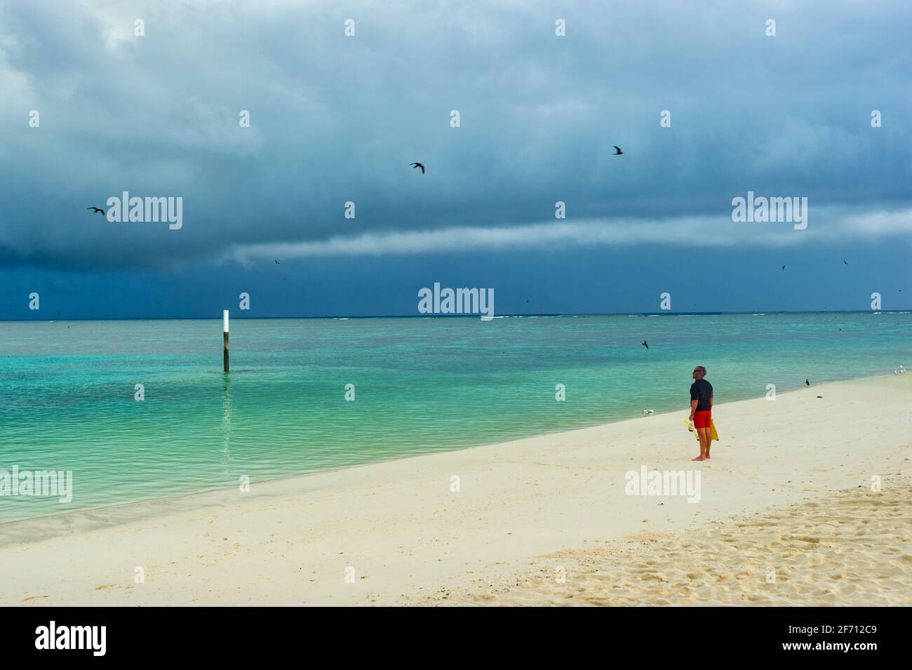 Tourist standing on the beach watching stormy skies over the Coral Sea at Heron Island, Southern Great Barrier Reef, Queensland, QLD, Australia Stock Photo