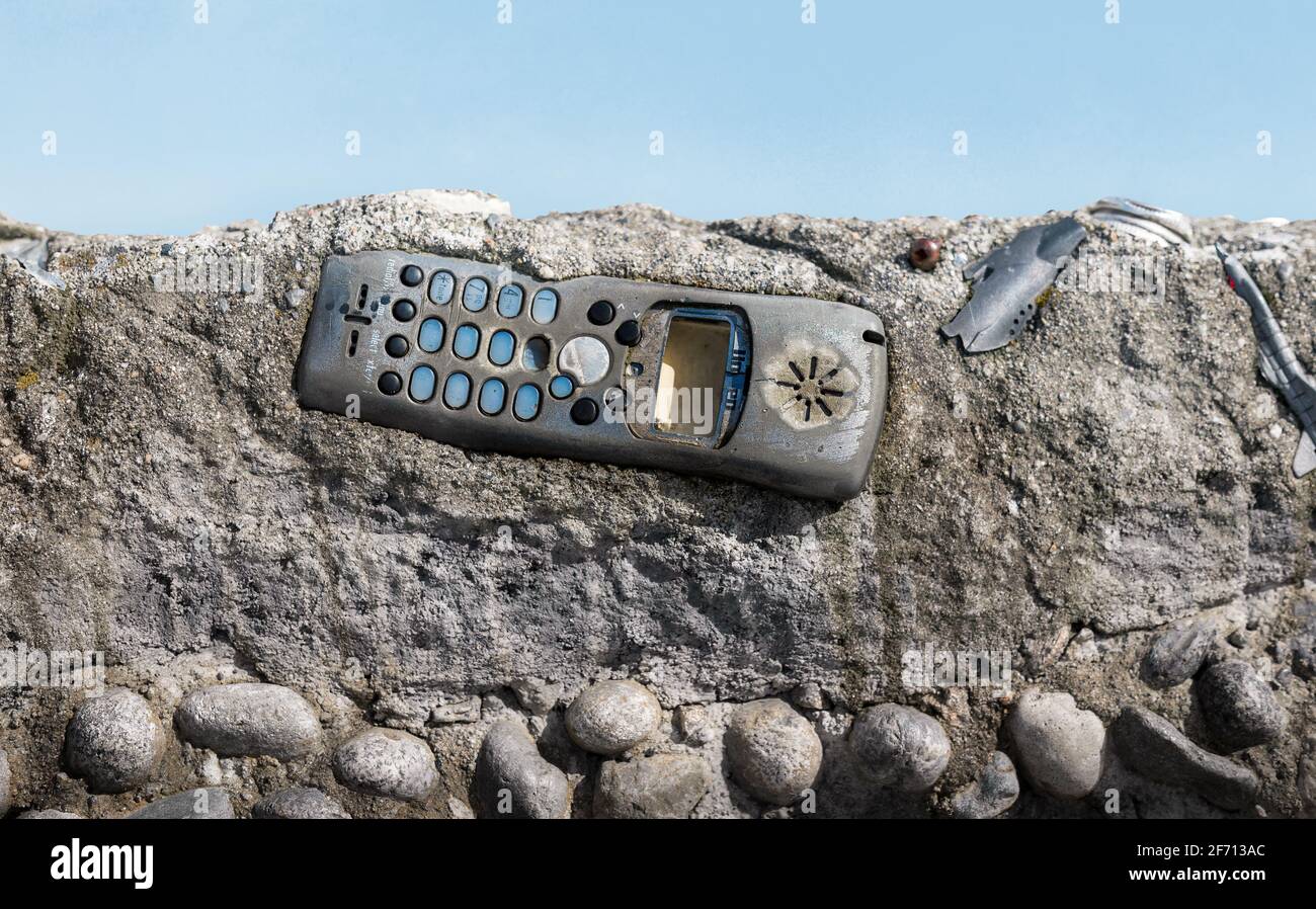 Old phone embedded in concrete layer with defocused landscape background. Human trash in ground sedimentation. Concept for non biodegradable materials Stock Photo