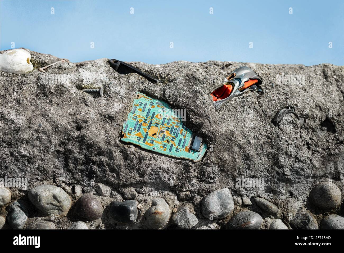 Harddrive embedded in concrete layer with other human debris. Day time