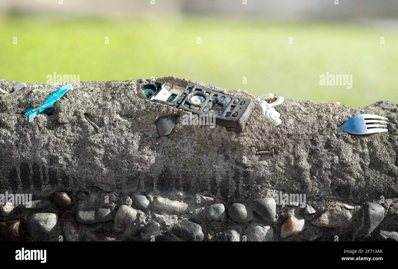Old phone embedded in concrete layer with defocused landscape background. Human civilization garbage in sedimentation. Concept for human impact on pla Stock Photo