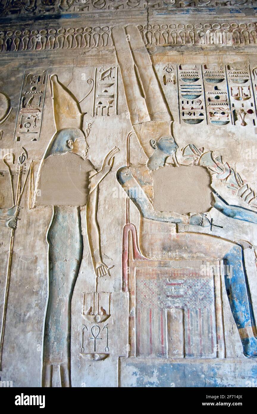 An Ancient Egyptian hieroglyphic carving showing the goddess Isis behind the seated king of the gods Amun Ra. This large coloured carving is on a wall Stock Photo