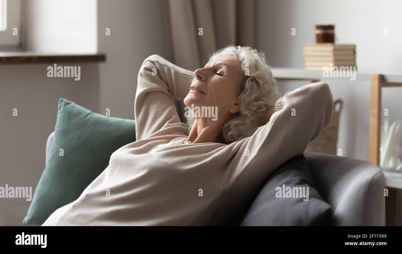 Peaceful older 60s lady resting on comfortable couch Stock Photo
